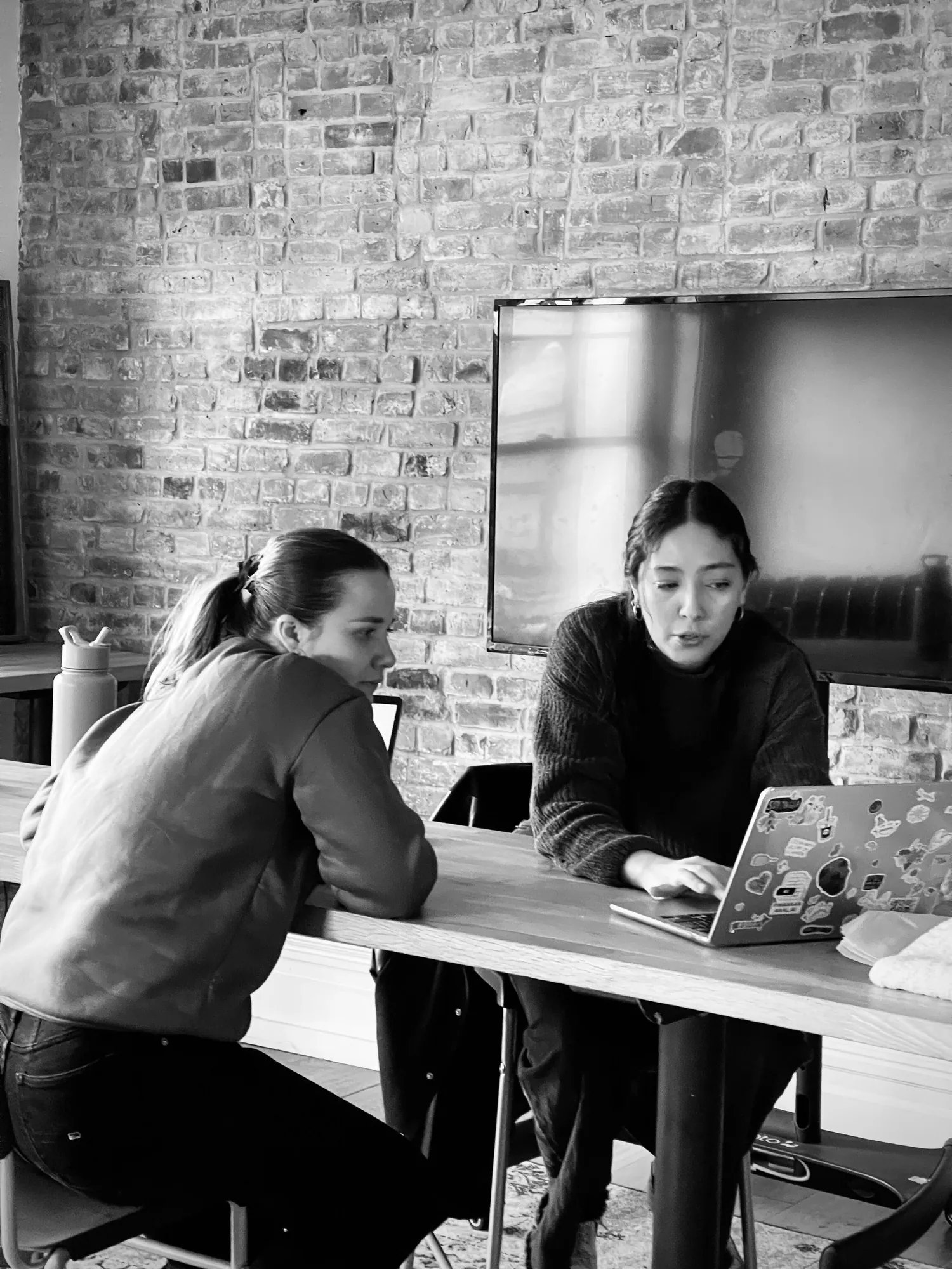 Sharing a laptop at the table by the brick wall